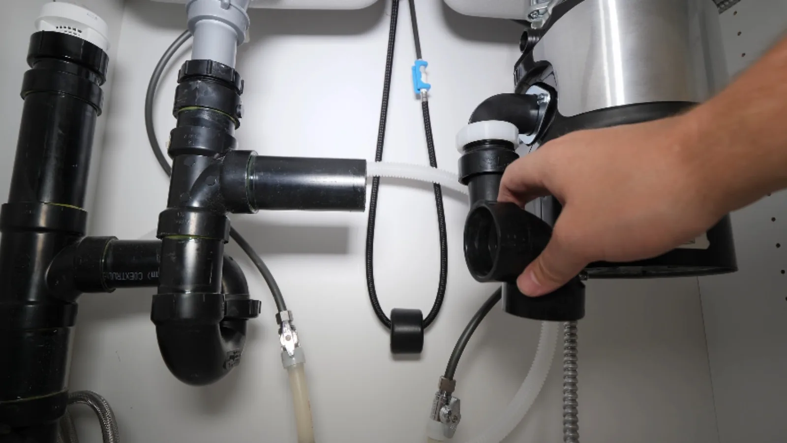 Hand working on a garbage disposal and drain pipes under a kitchen sink